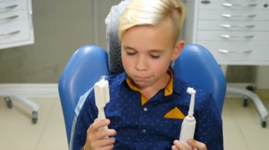 Elinde elektrikli diş fırçası olan gülümseyen çocuğun portresi. Kişisel ağız temizliği. Pediatrik dişçi ofisi. Modern dişçilik. 4k video