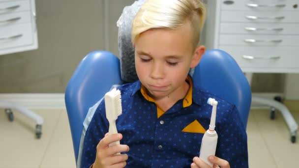 Porträt eines lächelnden Jungen, der im Zahnarztstuhl sitzt und eine elektrische Zahnbürste hält. Persönliche Mundhygiene. Kinderzahnarztpraxis. Moderne Zahnheilkunde. 4 k Video — Stockvideo