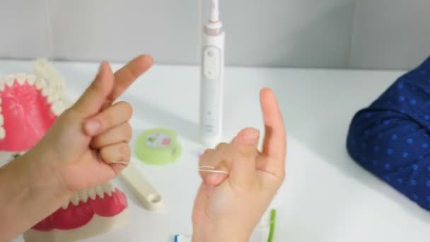 Ортодонт показывает, как чистить зубы с помощью зубной нити и модели челюсти. Руки держат нить для чистки зубов. Цветущие зубы. крупным планом. Гигиена полости рта. 4 k видео — стоковое видео