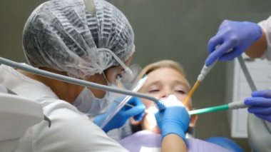 Diş tedavisi sırasında plastik kalkan takan kadın doktor, yüz koruma programındaki doktor: maske ve ekran. Küçük çocuk diş bakımı yaptırıyor. Yakın plan. 4k video