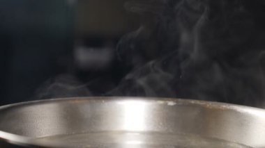 Buhar ya da Buhar bulutları fırındaki kızgın çelik tavadan yükseliyor. Yemek pişirirken tavadan buhar çıkıyor. Yavaş çekimde pişirme işlemi. Buhar ve beyaz duman siyah arkaplanda yükseliyor. Tam Hd