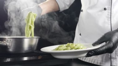 İtalyan restoranında makarna pişirmek. Şef tabakta makarna servis ediyor. Ağır çekim. Buhar ya da beyaz buhar siyaha yükseliyor. İtalyan mutfağı. Mutfak dilleriyle makarnayı tabağa koymak. Tam Hd