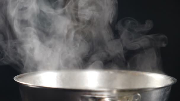 Chmury pary lub pary powstające z gotującej się stalowej patelni na kuchence. Para z patelni podczas gotowania. Proces gotowania w zwolnionym tempie. Para i biały dym narastają na czarnym tle. Pełny hd — Wideo stockowe