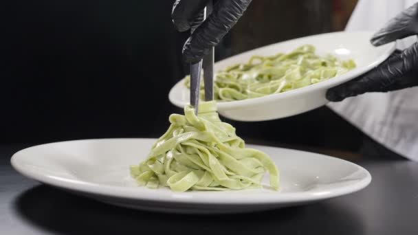 Cocinar pasta en restaurante italiano. Chef sirviendo pasta cocida en el plato. En cámara lenta. Vapor o vapor blanco subiendo sobre negro. Cocina italiana. Poner la pasta en el plato con las lenguas de cocina. Full hd — Vídeo de stock