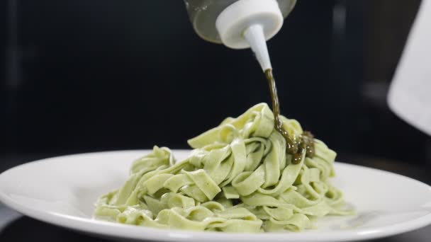 Pouring pesto sauce into plate with cooked pasta on black background. Slow motion. Cooking delicious meal. Italian cuisine. Chef serves dish in luxury restaurant. Full hd — Stock Video