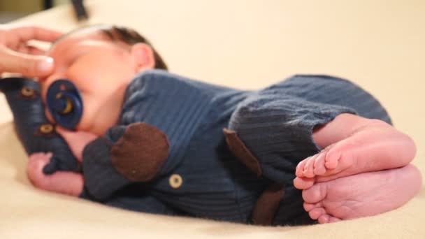 小さな愛らしい新生児の男の子は、布団を頭の下に、ニットのスーツを着たまま寝て横たわっています。鼻や頬に彼の肌に触れ、愛撫しながら、かわいい幼児の睡眠。四キロ — ストック動画