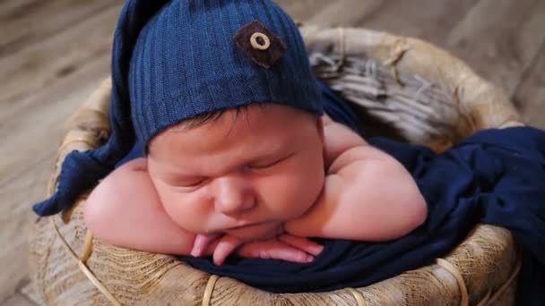 Очаровательный, милый и трогательный 10-дневный новорожденный мальчик спит в плетеной корзине в фотозоне, гримасит, зевает и корчит рожи. Детство, младенчество, отцовство, материнство. 4 k видео — стоковое видео