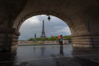 Genç Çift köprü altında duran ve Eyfel Kulesi kırmızı şemsiye ile seyir paris, Fransa