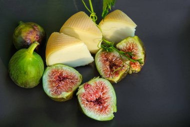Kahverengi bir yüzeyde peynir ve incir parçaları. Dilimlenmiş incirler üzerinde güneş ışınları. Provence.