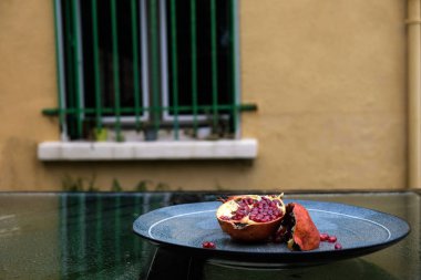 Seramik tabakta kırık nar meyvesi. Cam yüzeyde. Açık havada. Evin penceresinin önünde. Provence'da yağmurda.