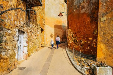  Roussillon Provence Fransa. 9 Şubat 2019. Turistik köyü. Koyu sarı renkli evler. Bir kadın bir çocuk ile çan kulesi için turistik ileridebir tırmanıyor.