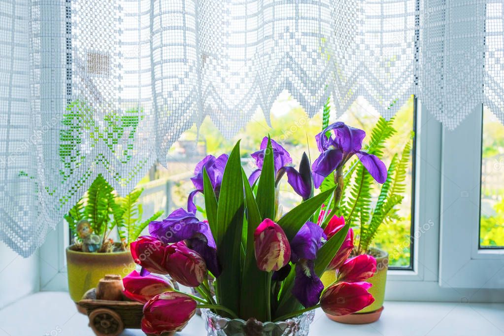 Bouquet of pink and purple flowers on the window sill with white curtains. Cozy light room in a country house in Ukraine.