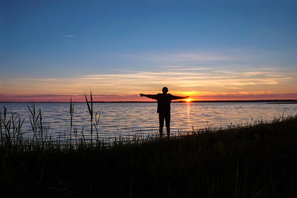 The man 58 years old on the shore of Svityas Like admires the sunset in the summer in Ukraine. The man extended his arms wide.