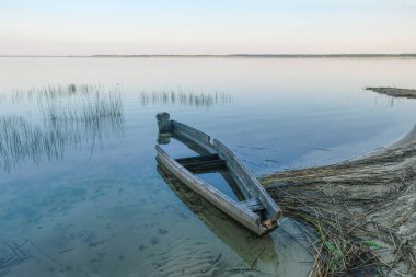 Büyük bir gölün kumlu kıyısında eski bir ahşap tekne. Svityaz Gölü 'nde gündoğumu. Ukraynalı doğa. Boşluk Kopyala.