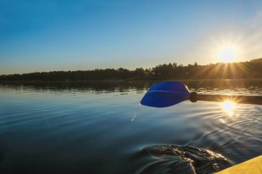 Sakin bir gölün ve yükselen güneşin arka planında mavi bir kürek parçası. Sağlıklı yaşam tarzı. Kopyalama alanı.