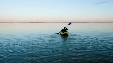 Güneşin doğuşuyla arka planda kayıkta 58 yaşında bir adam. Ukrayna'da su turizmi.