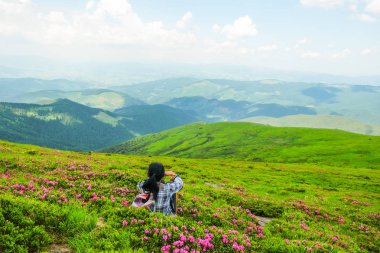 Mutlu kadın 59 yaşında Karpatdağları'nda Alp çayırlarında Rhododendron çiçekleri arasında oturur. Ukrayna turizmi. Arkadan görüntüle.