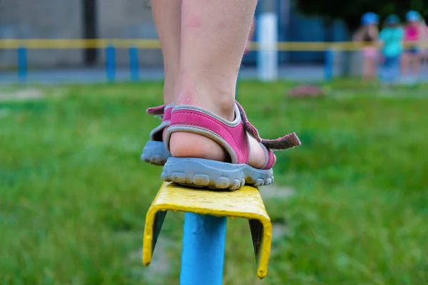 Baby feet in sandals on a sports equipment for balance. Children\'s playground in summer in Ukraine.
