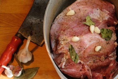 Dökme demir bir tencerede marine jambon parçası. Ahşap bir yüzeyde bir helikopter ve sarımsak var..