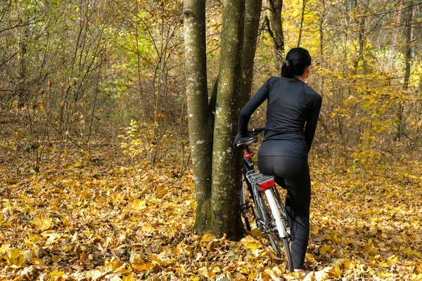 58 year old woman in black clothes with beautiful silhouette near bicycle on yellow autumn background. Woman with her back turned. Copy space.
