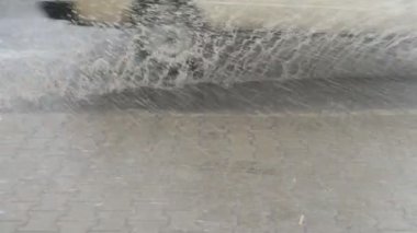 Bir fırtına sırasında yolda su akışı ve su tozu. Su akıntılarını kesen araba çarkları. Kaldırıma su sıçrıyor..