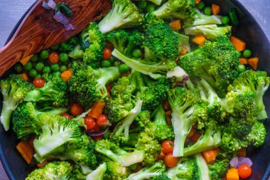  Taze düşük kalorili brokoli, havuç, yeşil bezelye, domates tavada pişirilir. Uygun beslenme konsepti. Ev yapımı yemek konsepti. Mutfak spatulasında bir yunus silueti..