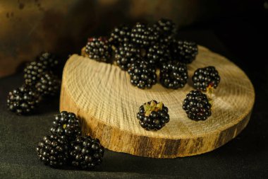 Dağıtılmış böğürtlenler ahşap bir dilim üzerinde. Koyu resim.