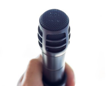 Şık siyah mikrofon açık beyaz boşluk önünde bir stand. Beyaz bir erkek el mikrofon tutuyor.