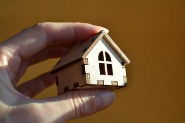 Kız el ahşap minyatür oyuncak ev güneş ışığı sarı arka plan ile tutarak