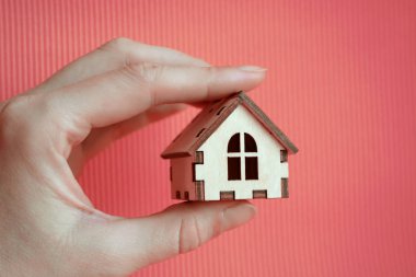 Kız el ahşap minyatür oyuncak ev güneş ışığı ile pembe bir arka plan üzerinde tutarak