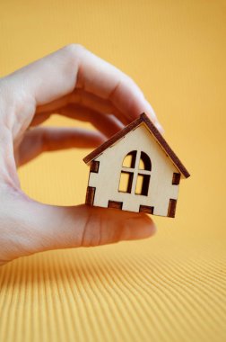 Man hand holding wooden miniature toy house on yellow background, vertically oriented
