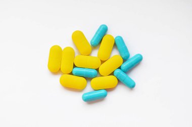 Yellow oval pills and blue capsules on white background top view