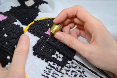 Kadın el ile siyah ve pembe yün iplik içinde sarı çember, beyaz kumaş üzerine nakış iğne ile embroiders.