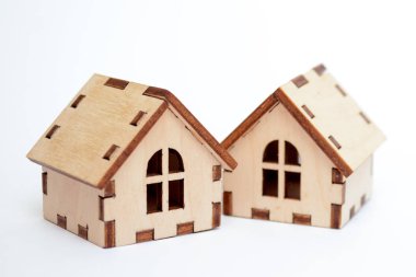 Beyaz bir arka plan üzerinde iki ahşap oyuncak ev, bir evin arkasında diğer, kavramı evleri satmak için standları
