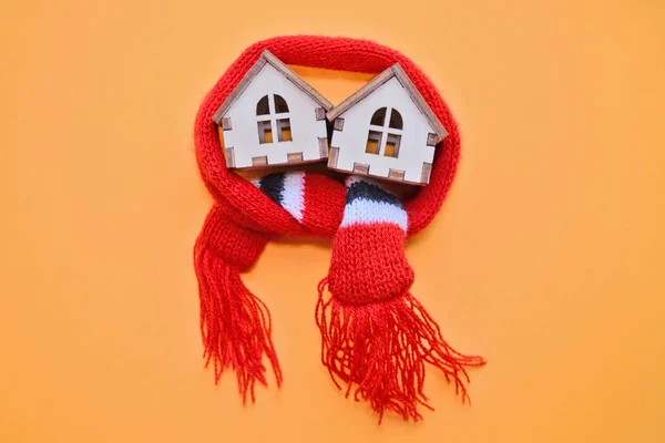 Two wooden toy houses with windows in red scarf on a orange background, warm house, insulation of houses, copyspace