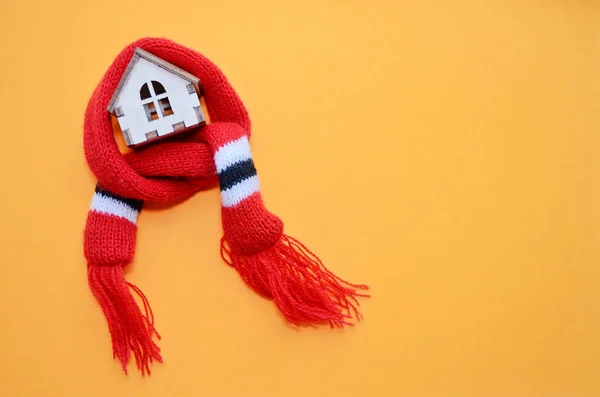 Wooden toy house with windows in red scarf on a orange background, warm house, insulation of houses, copyspace