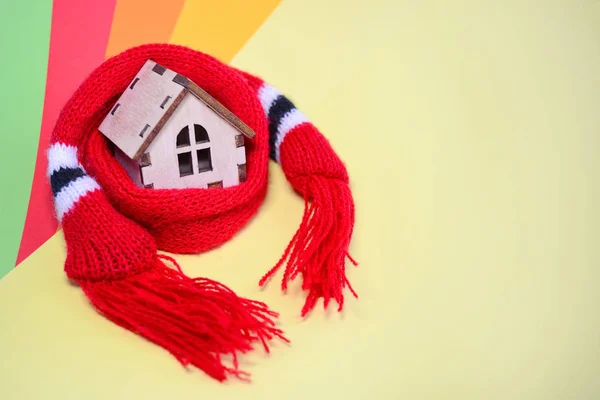 Wooden toy house with windows in a red scarf on a rainbow colored background, warm house, insulation of houses, closeup