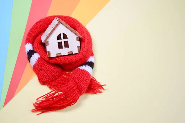 Wooden toy house with windows in a red scarf on a rainbow colored background, warm house, insulation of houses, copyspace