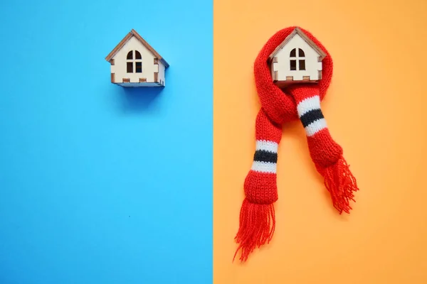 Two wooden toy houses on blue and orange background, one house weared on scarf, concept for insulation houses with copyspace, cold and warm house