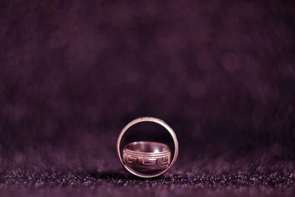 Two silver vintage wedding rings on a black and pink shiny surface, with a blurred background and space for text