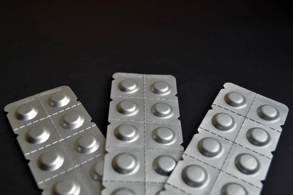 Round medical tablets in three packs, tablets packed in blisters on the lower side, with copyspace on black background