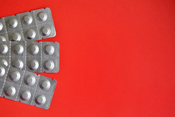 Round medical tablets in three packs, tablets packed in blisters on the left side with copyspace on red background