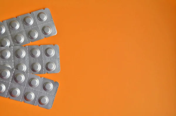 Round medical tablets in three packs, tablets packed in blisters on the left side with copyspace on orange background