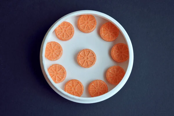 Orangefarbene runde Tabletten in Form einer Orange liegen in einem runden weißen Glas wie eine Uhr auf schwarzem Hintergrund mit Kopierraum — Stockfoto