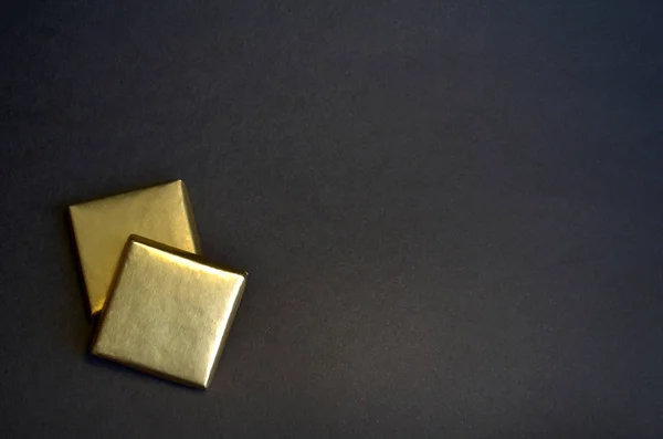 Dois pedaços quadrados de chocolate com folha dourada em um fundo preto com espaço para texto — Fotografia de Stock