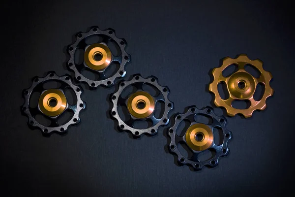 Color rollers, black, golden gears for bicycle rear derailleur on black background