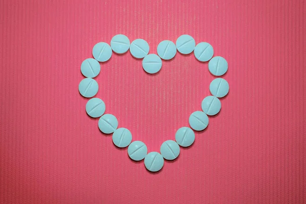 Masse blå, glatte, konvekse tabletter med strimler på rosa, stripet bakgrunn, i form av hjerte – stockfoto