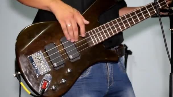 Guitarrista toca en un bajo marrón en el estudio, vestido con jeans y una camisa negra — Vídeos de Stock