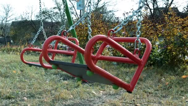 Parque infantil en verano con el columpio rojo, que está vacío y balanceándose — Vídeos de Stock