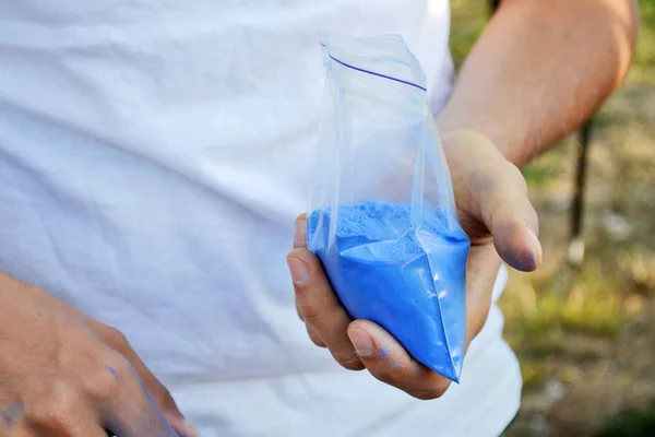 Paquete con polvo azul para la guerra del holi en las manos de un hombre en camisa blanca — Foto de Stock